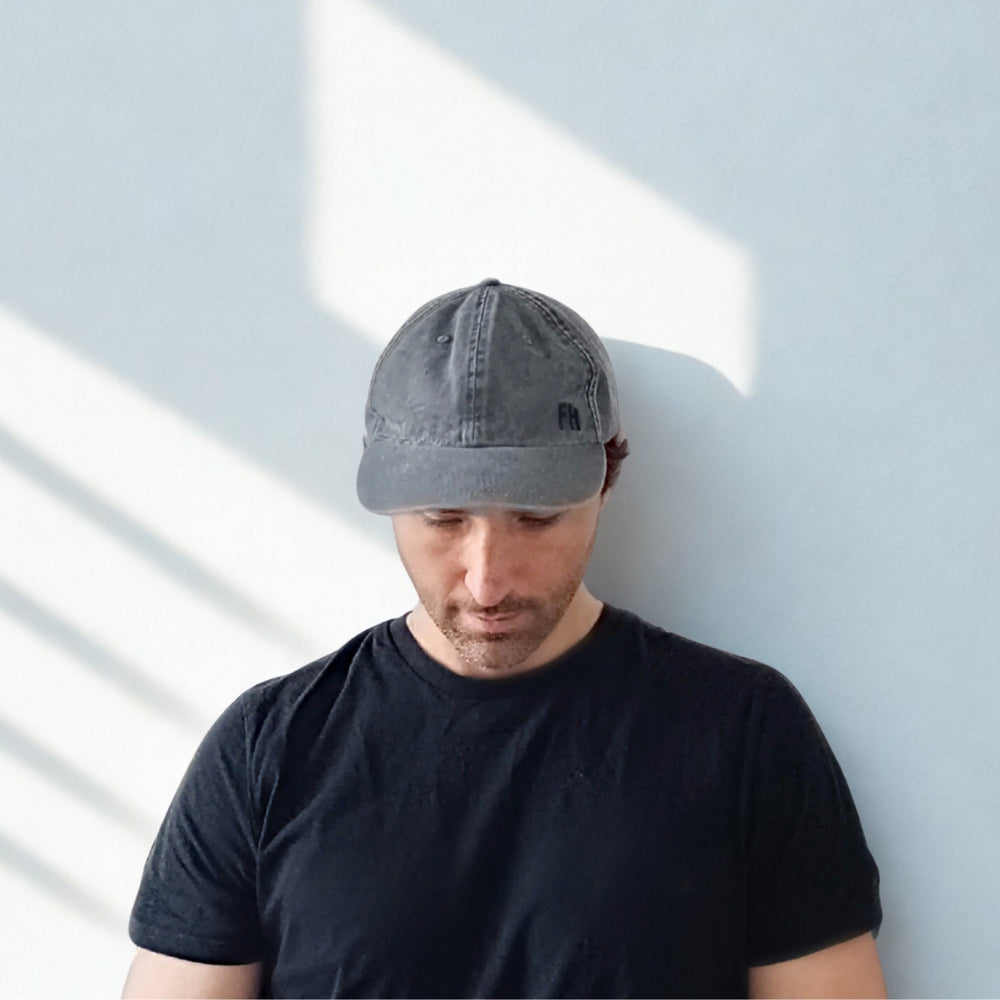Homme portant une Casquette Dad Hat XL gris foncé contre un mur clair avec des ombres.